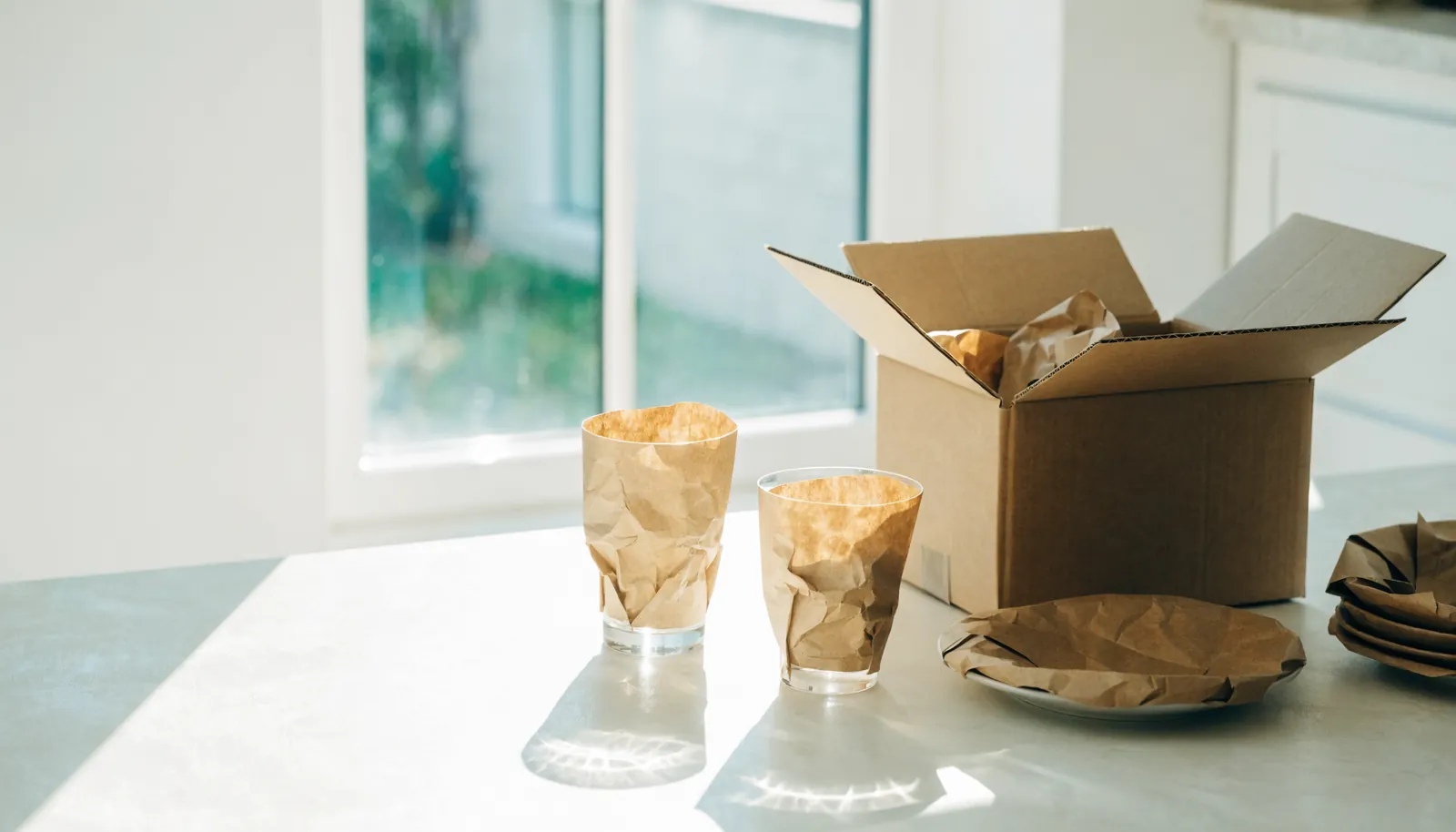 Küchenarbeitsplatte im Tageslicht, Gläser in Packpapier gewickelt, daneben ein halb gepackter Karton