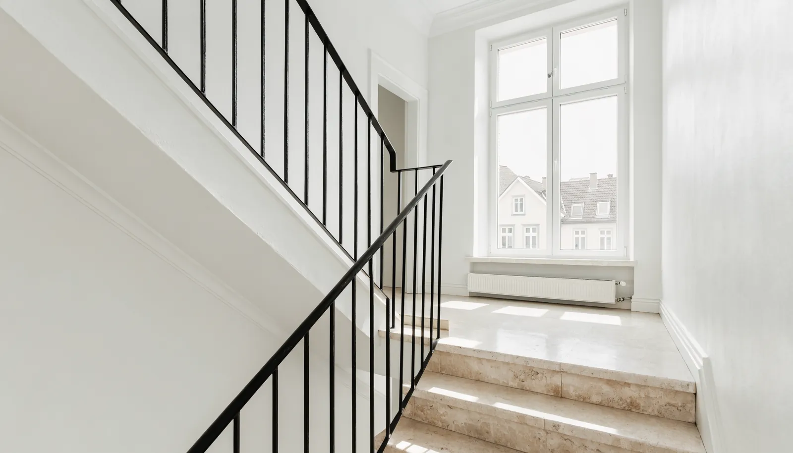 Helles Altbau-Treppenhaus mit breiten Stufen und schmalem Eisengeländer